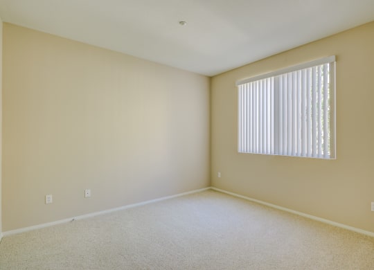 a bedroom with a large window and beige walls  at Tesoro Senior Apartments, California, 91326