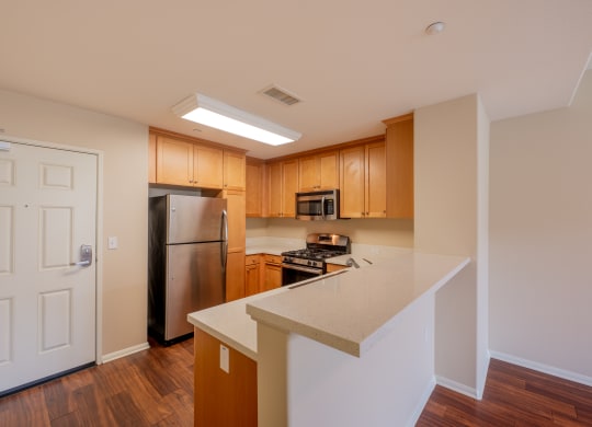 a kitchen with wood cabinets and a white counter top and breakfast bar at Ventana Senior Apartments, Northridge