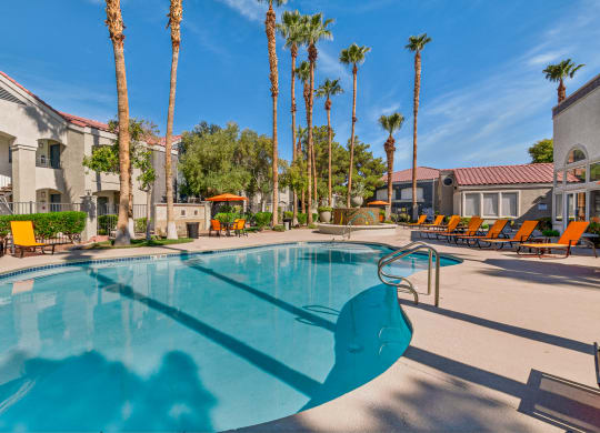 a swimming pool with yellow chaise lounge chairs and palm trees in the background at Rancho Serene, Las Vegas, NV