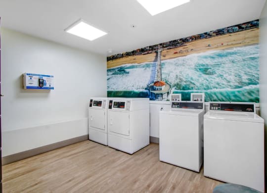a laundry room with four washers and a painting of a beach on the wall at The Kenmore Los Feliz, Los Angeles, CA