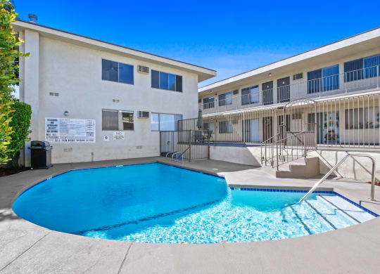 our apartments have a large swimming pool and a building with a fence at Palm Capri Apartments, California, 91501