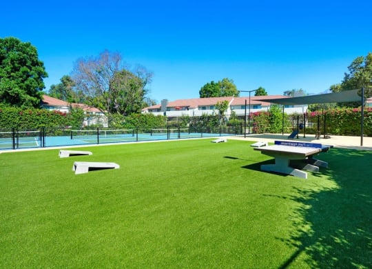 a picnic table and ping pong table sit in the middle of a grassy area at The Park Apartments, California