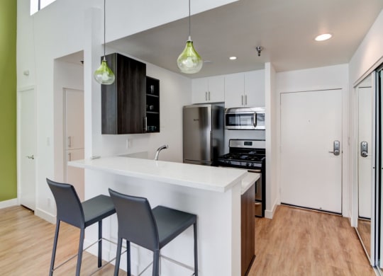 a kitchen with white cabinets and a white counter top with three stools in front of it  at El Greco Lofts, Los Angeles, CA, 90024