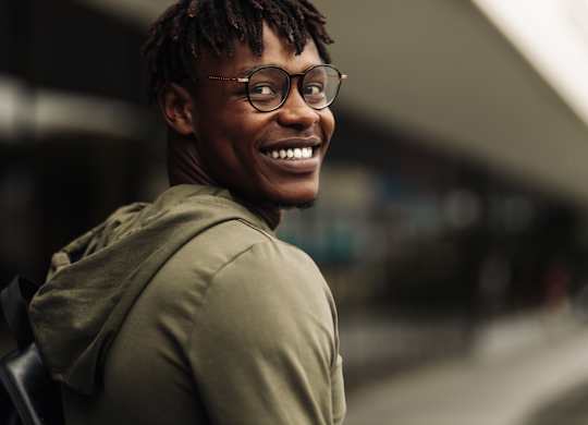 A man with dreadlocks and glasses is smiling.