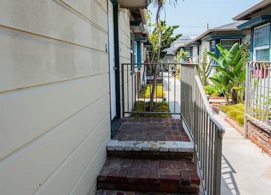 A small brick walkway leads to a door on a tan building.