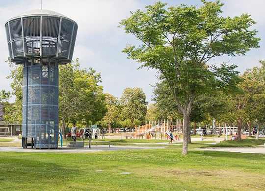 A large water tower in a park with trees and a playground.