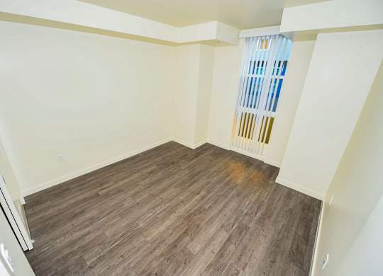 A room with wooden flooring and a window with a blue curtain.