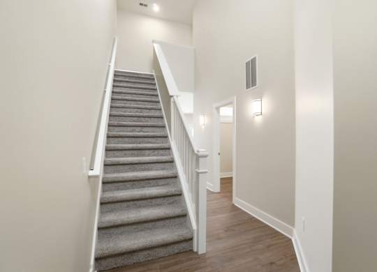A staircase with a grey carpeted runner and white balusters.