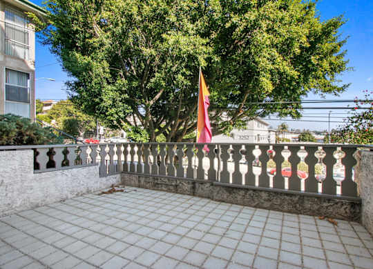 A balcony with a flag and a tree in the background.