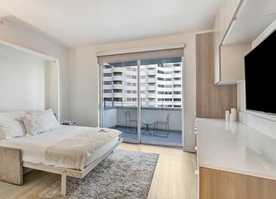A bedroom with a bed, a chair, and a window with blinds.at Wilshire Margot, Los Angeles 