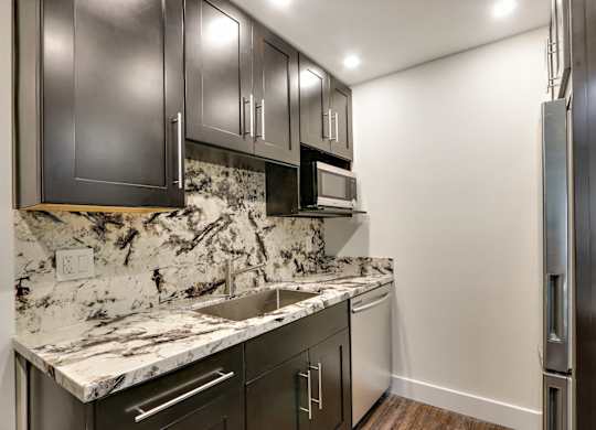 Kitchen with granite countertops and backsplash, stainless steel dishwasher, dishwasher, dark brown kitchen cabinets, wood style floors, two door refrigerator.