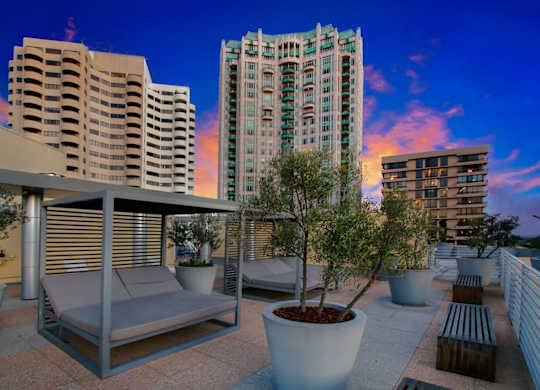 A patio with a couch, table, and potted plants with buildings in the background.at Wilshire Margot, California