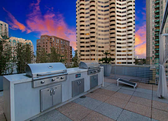 A BBQ grill is on a patio with a cityscape in the background.at Wilshire Margot, Los Angeles