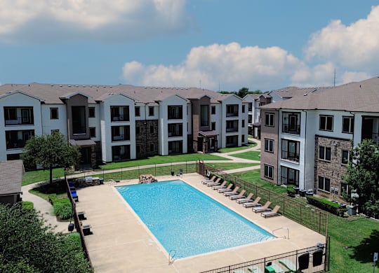 A swimming pool is surrounded by lounge chairs in a residential complex.
