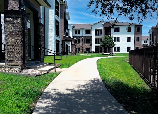 A long concrete walkway leads through a grassy area between two rows of apartment buildings.