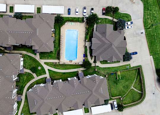 A bird's eye view of a residential area with houses, a swimming pool, and a parking lot.