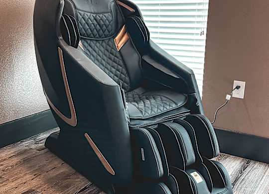A black massage chair with a wooden base is placed in a room.