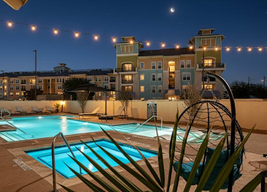 A pool area with a building in the background and lights strung above.