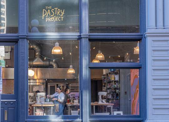 a woman stands in the window of a pastry shop