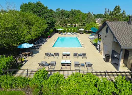 A pool surrounded by chairs and trees.