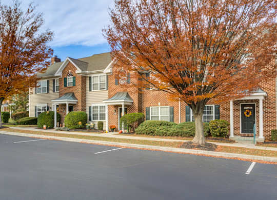 A tree with orange leaves stands in front of a brick house at Highlands at Warwick Apartments, Pennsylvania 17543