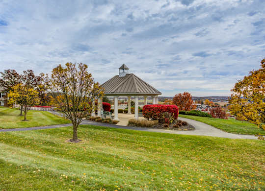 A gazebo sits in the middle of a grassy area with trees and a house in the background at Highlands at Warwick Apartments, Lilitz
