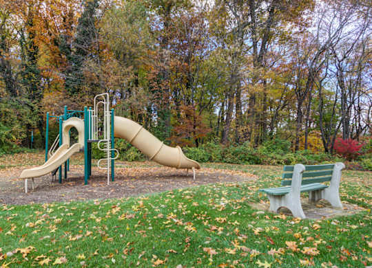 A playground with a yellow slide and two green benches at Highlands at Warwick Apartments, Pennsylvania 17543