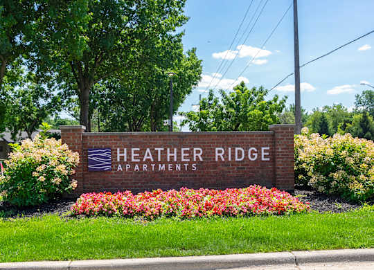 A sign for Heather Ridge Apartments is surrounded by flowers and greenery.