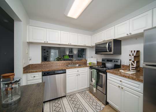 A kitchen with white cabinets and a patterned rug on the floor.