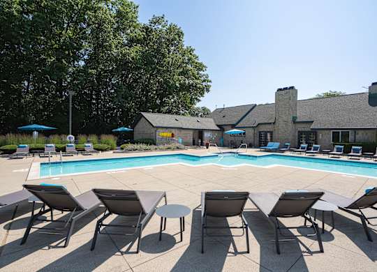 A pool surrounded by chairs and umbrellas with a building in the background.