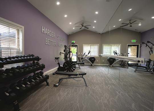 A gym with a purple wall and a sign that says "Harder, Stronger, Better Faster".