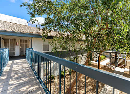 A balcony with a railing overlooks a courtyard with a tree and a building.
