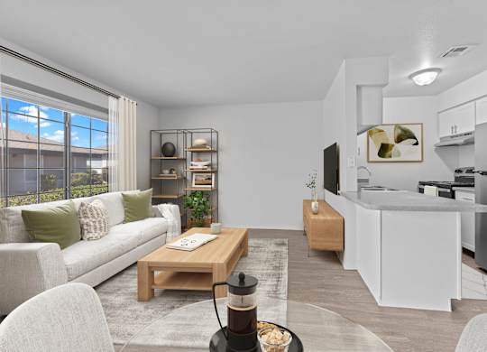 A modern living room with a white sofa, a wooden coffee table, and a kitchen area in the background.