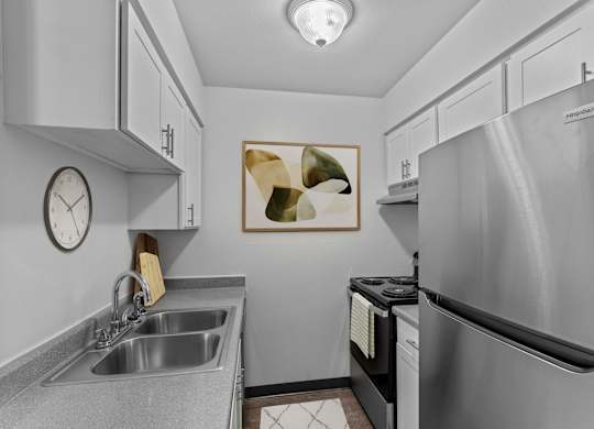 A modern kitchen with a stainless steel refrigerator, a sink, and a clock on the wall.