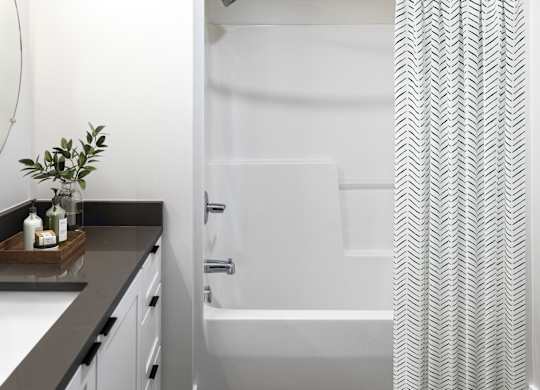 A bathroom with a white tub and a grey and white patterned shower curtain.