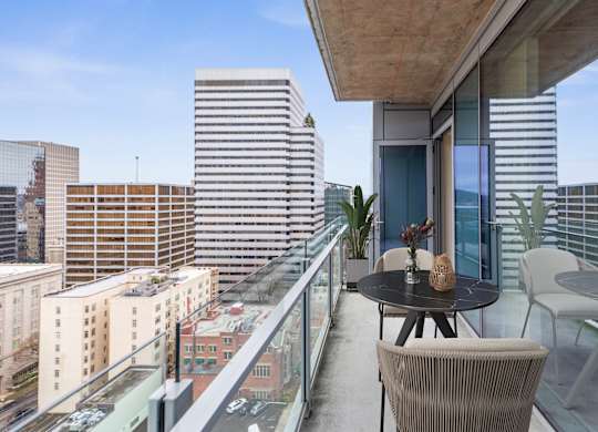 A balcony with a table and chairs overlooks a cityscape.