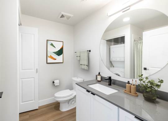 A bathroom with a toilet, sink, mirror, and a painting on the wall.