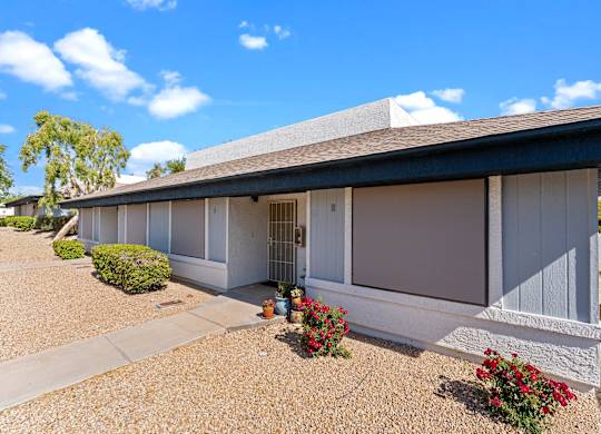 A house with a grey roof and white walls with a gravel driveway in front.
