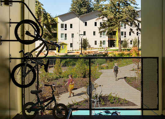 A bicycle is hanging on a rack in a room with a view of a courtyard.
