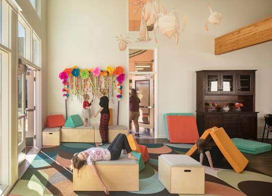 A woman is lying on a colorful mat in a room with children's play areas.