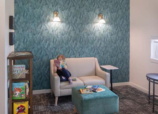 A doll is sitting on a chair in a room with a green wallpaper.