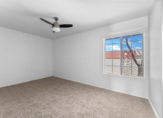 A room with a ceiling fan and a window showing a view of a building and trees.