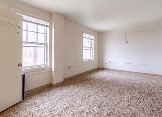 A room with a carpeted floor and two windows.