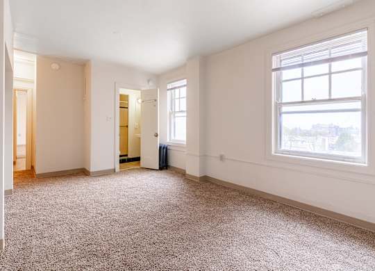 A large empty room with a carpeted floor and a window.