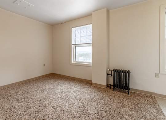 A room with a carpeted floor, a window, and a radiator.