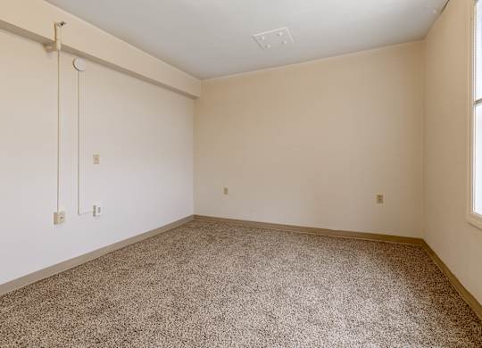 A room with a carpeted floor and a window on the right side.