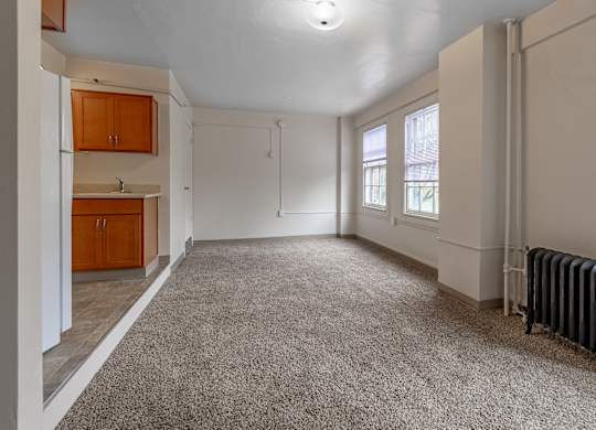 A spacious room with a carpeted floor and a radiator on the wall.