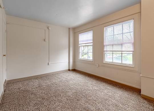 A room with a carpeted floor and two windows.