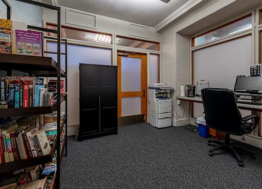 A room with a bookshelf, a desk with a computer, and a black office chair.