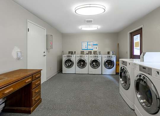 A laundry room with a row of washing machines and a wooden cabinet.
